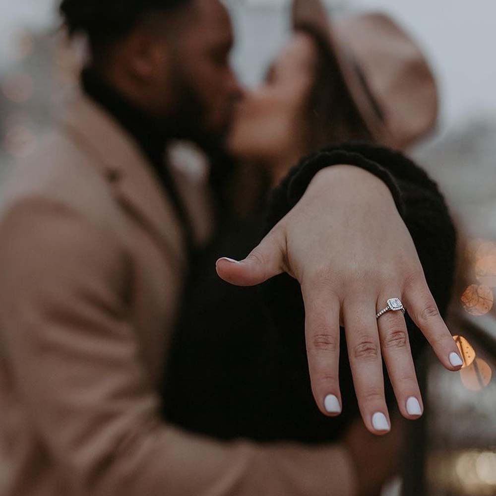 A blurred photo of a couple kissing with her hand and diamond engagement ring in focus 
