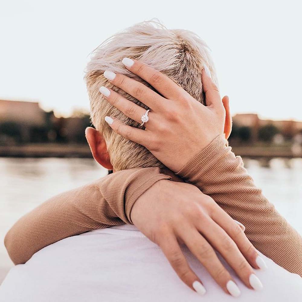 Couple facing away from the camera, her hands are wrapped around his head, her engagement ring on full display