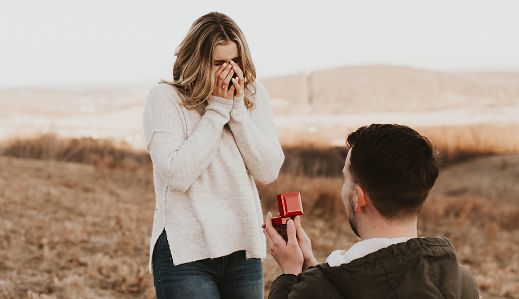 A man proposing to a woman while holding a red James Allen ring box 