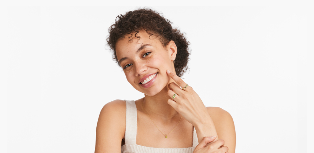 A model smiles while showing off two rings from Blue Nile containing the August birthstone, peridot.