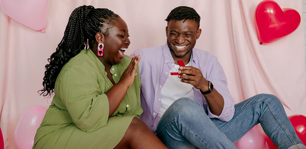A joyful couple sitting together as one partner opens a ring box, capturing a warm and candid moment that reflects how to announce an engagement.