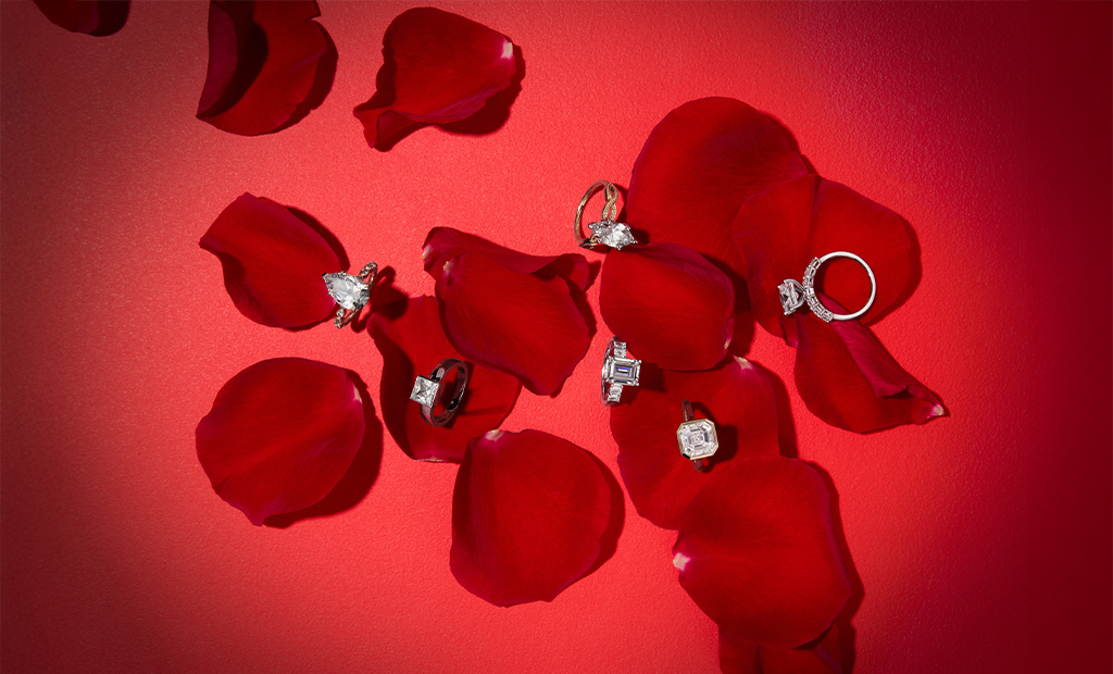 Assorted diamond engagement rings from James Allen's Valentine’s Day launch, scattered among red rose petals. 